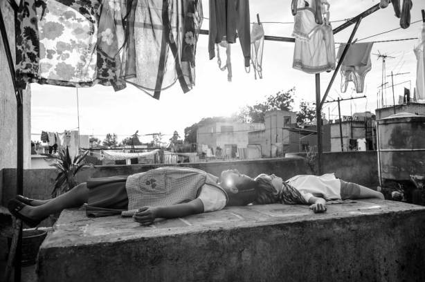 An still image from the film Roma showing a woman and boy lying down under a washing line and looking up at the sky